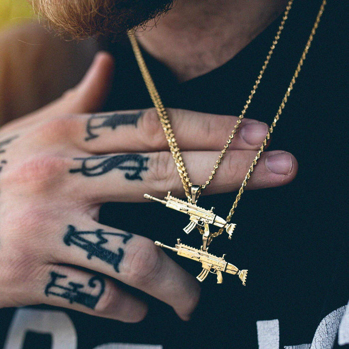 Two SCAR Gun Pendants in yellow gold, one on a 20” Ball Chain and the other on a 24” Rope Chain worn by a male model in a black graphic tee.