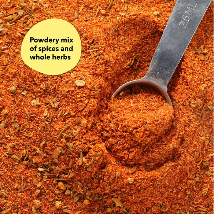 Overhead close-up of a dark reddish-brown spice blend with a dark metal spoon; a callout label reads Powdery mix of spices and whole herbs