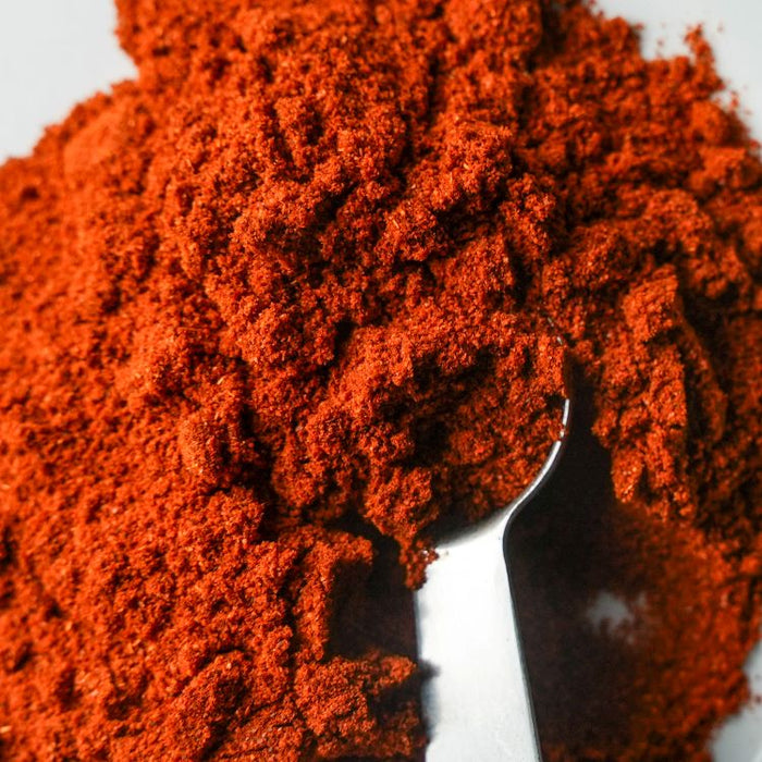 Close-up of red chili powder with a spoon on a white background