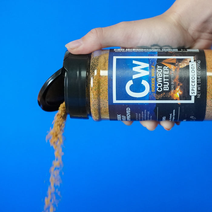 Hand holding a bottle of Cowboy Butter seasoning against a blue background