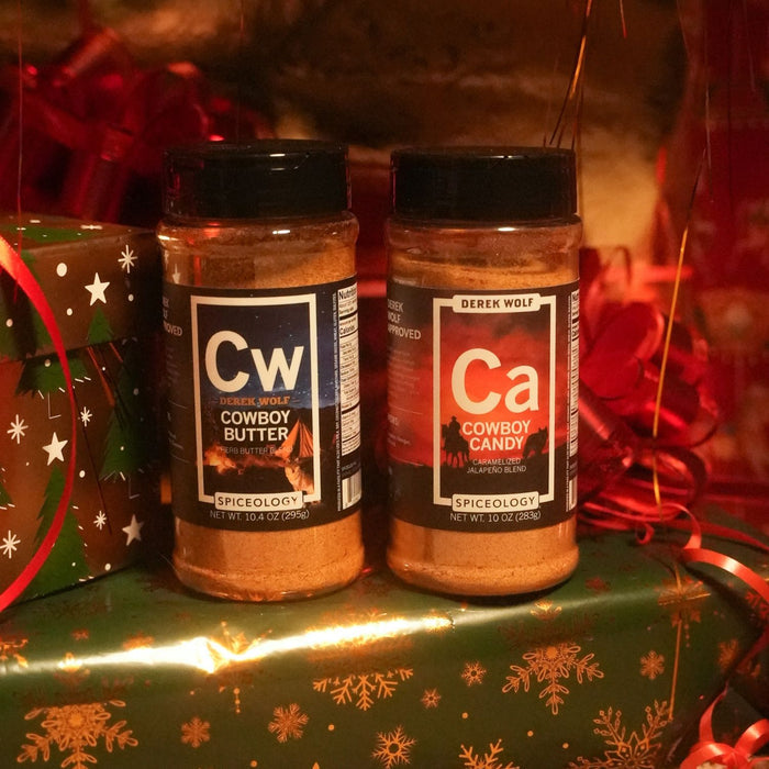 Two spice jars labeled 'Cowboy Butter' and 'Cowboy Candy' on a gift box with Christmas decorations.