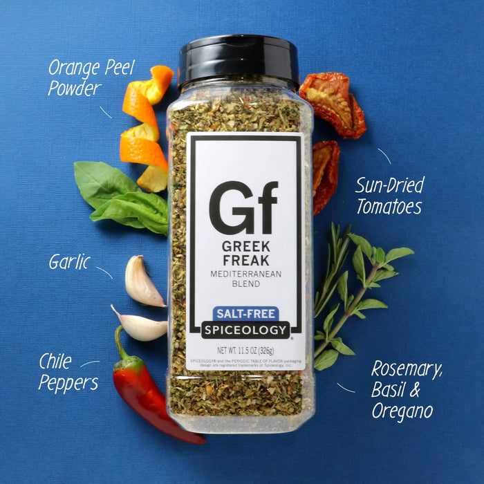 Spiceology Greek Freak Salt-Free shaker jar on a blue background with labeled ingredient callouts for Orange Peel Powder, Sauteed Tomatoes, Garlic, Chile Peppers, and Rosemary Basil and Oregano; fresh vegetables surrounding the jar