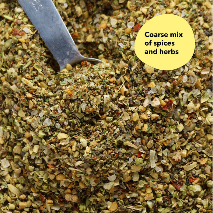 Overhead close-up of a coarse herby green and tan spice blend with a silver measuring spoon; a callout reads Coarse mix of spices and herbs