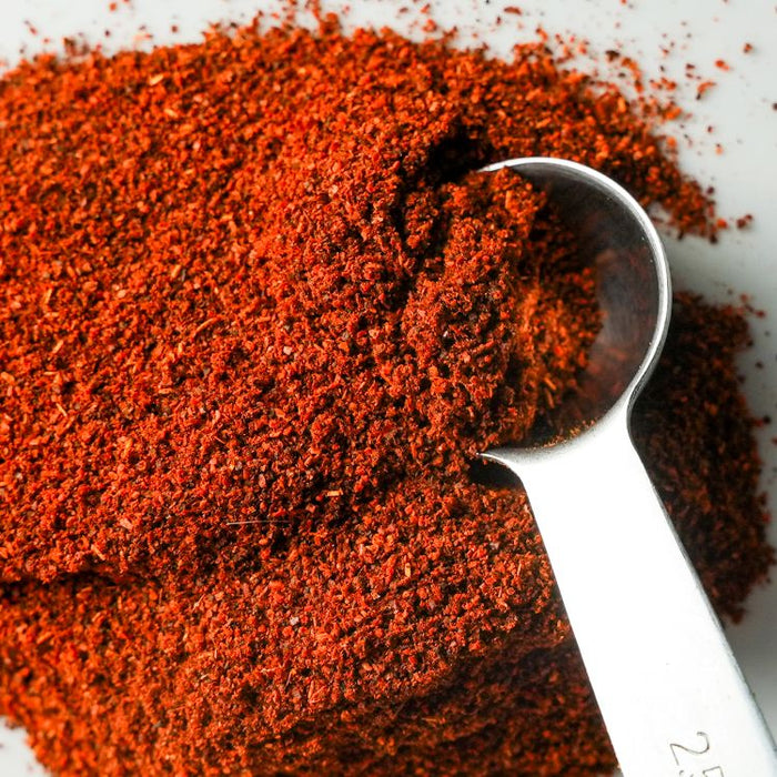 Close-up of red chile powder with a spoon on a white background