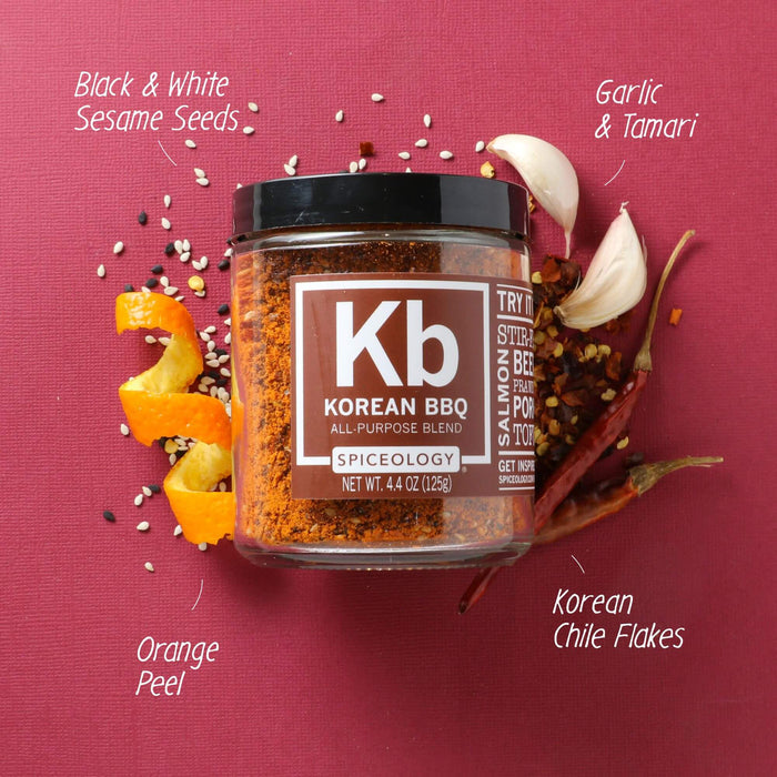 Jar of Spiceology korean bbq on a dark pink background with orange peel, korean chile flakes, garlic, tamari, and black and white sesame seeds