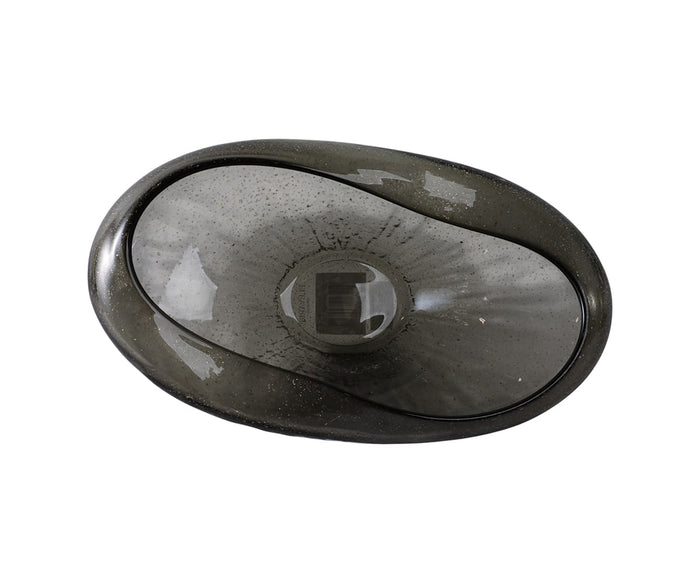 The Midnight Wave Bowl is a dark, oval-shaped glass bowl with a smooth, slightly translucent surface and hand-finished details for a distinctive texture. Captured from above on a white background, this elegant piece exemplifies modern organic decor.