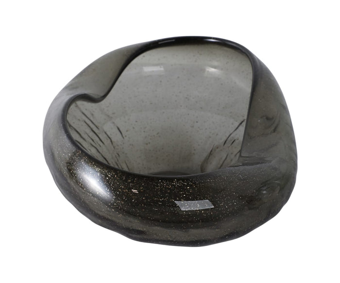 The Midnight Wave Bowl—a dark, irregularly shaped hand-finished glass piece with a smooth, glossy surface and speckled details—rests on a white background, making it a striking accent that effortlessly complements modern organic decor.