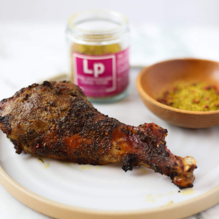 Turkey Legs 3 Ways closeup of a turkey leg seasoned in Pink Peppercorn Lemon Thyme with a dish and jar of Spiceology Pink Peppercorn Lemon Thyme on a white plate