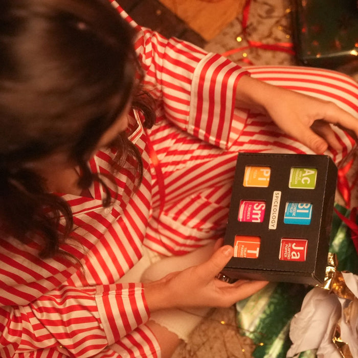 Person in red and white striped pajamas holding Spiceologys popcorn seasoning gift set box with colorful labels.