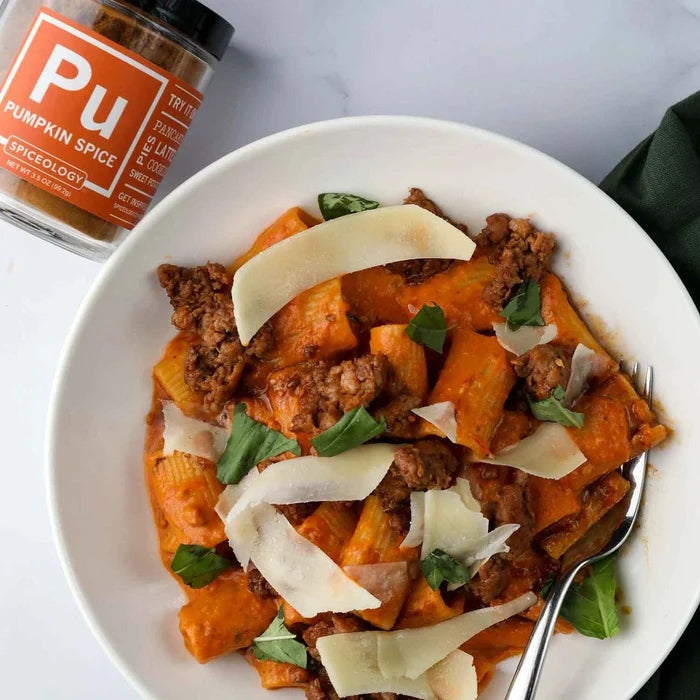 Pumpkin Spice Alla Vodka with Spicy Sausage featuring pumpkin puree, tomato and shallots, and the garlic, fresh herbs and Spiceology pumpkin spice blend topped with spicy Italian sausage and a glug of red wine in a white bowl with a jar of Spiceology Pumpkin Spice in the background