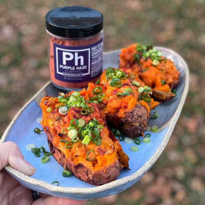 Purple Haze Twice-Baked Sweet Potatoes garnished with bacon and green onions on a blue plate next to a jar of Spiceology Purple Haze