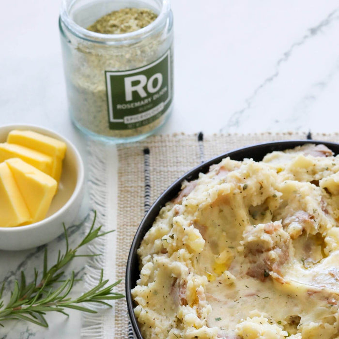 Rosemary Dijon & Garlic Mashed Red Potatoes in a bowl next to a dish of sliced butter and jar of Spiceology Rosemary Dijon