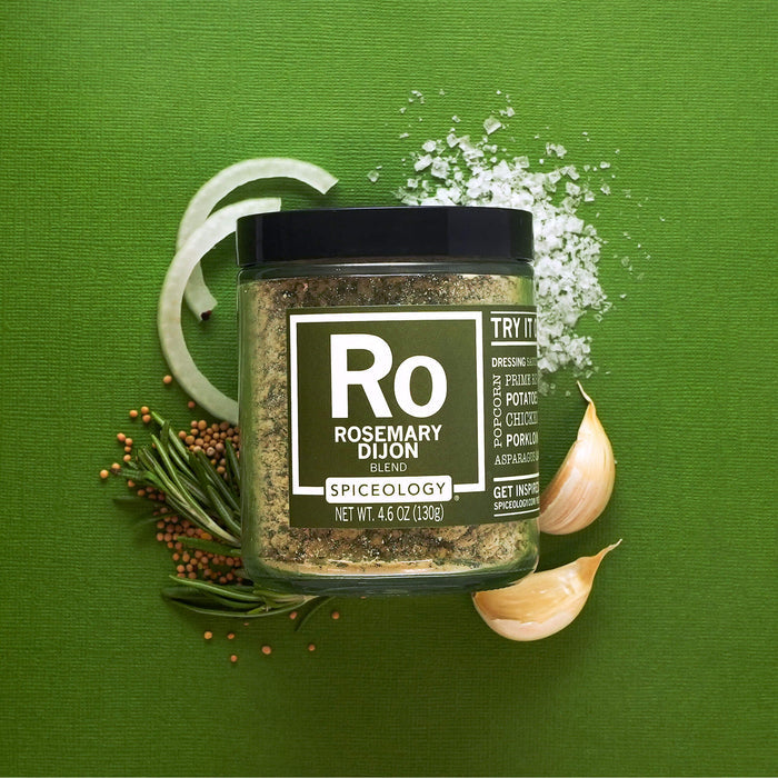Jar of Spiceology rosemary dijon on a green background with mustard seeds, garlic cloves, onion and salt