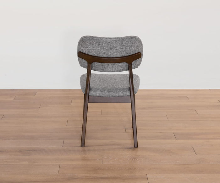 The Severin Dining Chair, featuring a dark gray upholstered seat and backrest and supported by sturdy rubberwood legs, is viewed from behind as it sits on a light wood floor against a plain white wall.