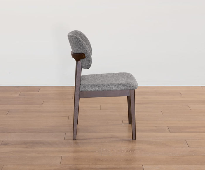 Side view of the Severin Dining Chair in dark gray modern upholstery, showcasing its wooden legs and frame, set on a light brown wooden floor against a plain white wall.
