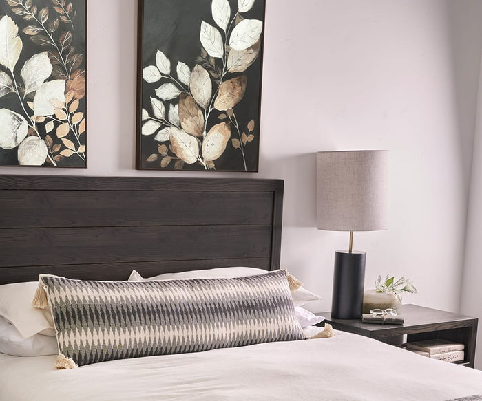 A neatly made bed with a long patterned pillow and a dark wooden headboard sits beneath the Silent Grove I & II Wall Art Set. A lamp, small plant, and stacked books rest on the bedside table against a light-colored wall.