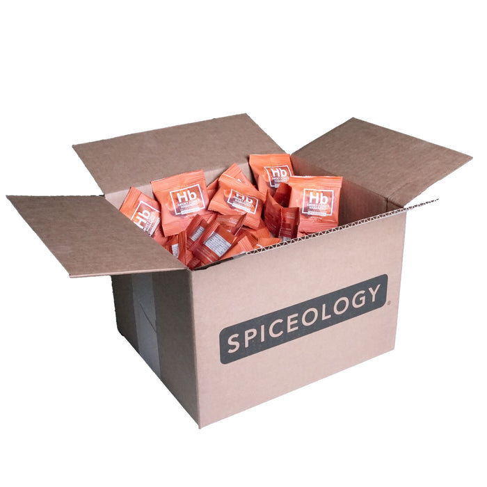 Cardboard box labeled 'Spiceology' filled with Smokey Honey Habanero packets on a white background