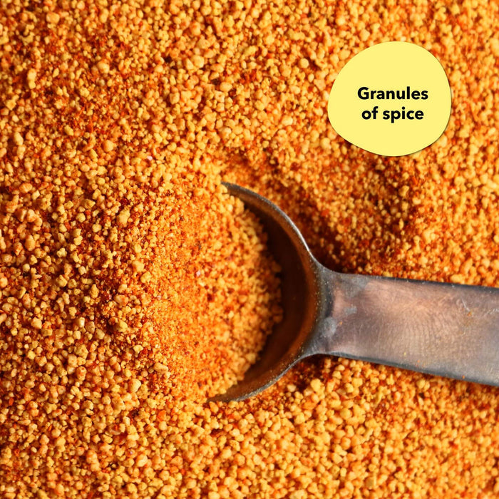 Overhead close-up of a reddish-orange granular spice blend with a dark metal spoon; a callout reads Granules of spices