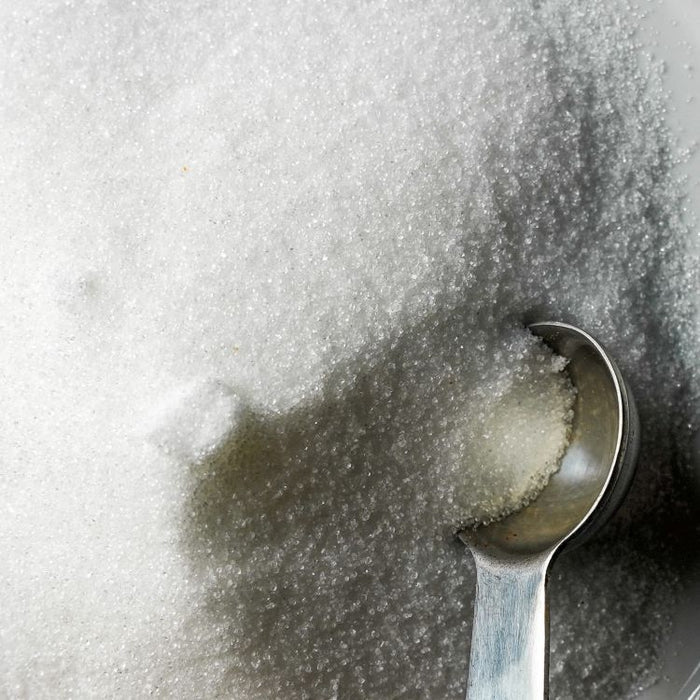 Spoon scooping sugar from a pile of granular white sodium citrate