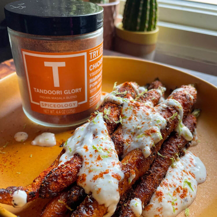 Tandoori Glory Roasted Carrots with Maple Yogurt featuring roasted and seasoned carrots drizzled in maple yogurt on a yellow plate  next to a jar of Spiceology Tandoori Glory