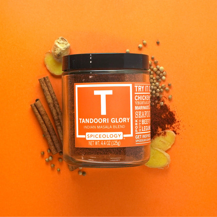 A jar of Spiceology Tandoori Glory on an orange background with cinnamon sticks, ginger, coriander ginger and dark red spice pile