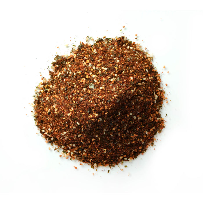 Closeup of coarse spice blend with a deep reddish-brown color, featuring chili, toasted seeds, and herbs