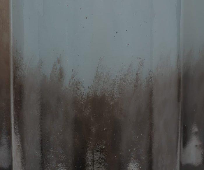 A close-up of a fogged, hand-finished glass with condensation and streaks of water, revealing smudged dark patterns and blurred reflections reminiscent of the surface of the Twilight Vase.